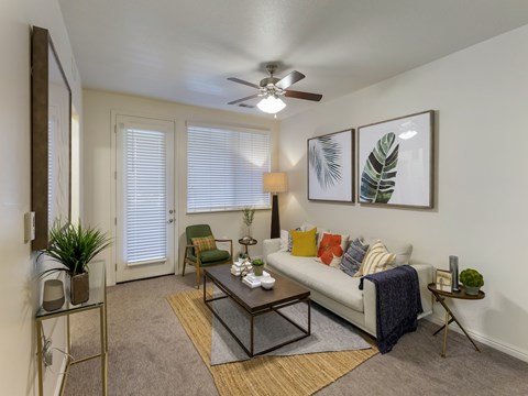 A living room with a white couch, a glass coffee table, and a ceiling fan.
