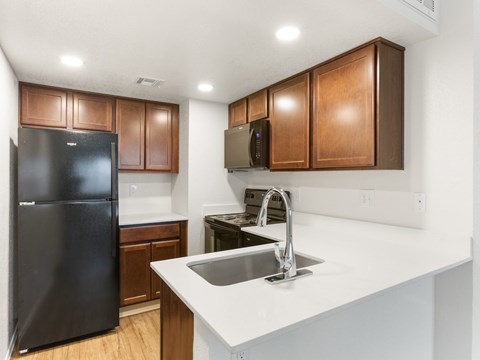 A kitchen with a black refrigerator and brown cabinets.