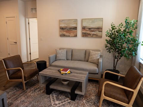 A living room with a grey couch, two chairs and a coffee table.