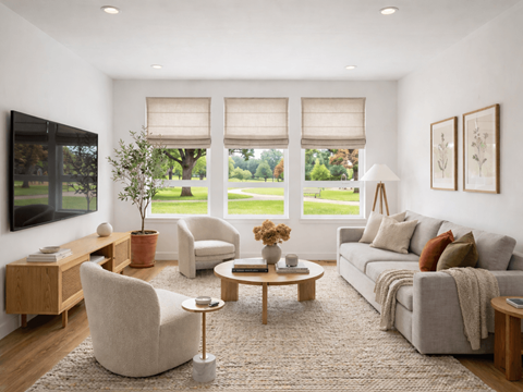 A living room with a grey couch, a wooden coffee table, and a large window with blinds.