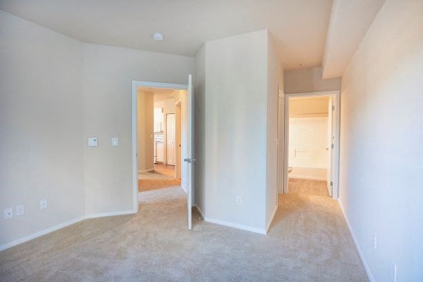 Bedroom interior with wall to wall carpet, two closets with french doors, two night stands with lamps, and art work hanging above the bed at Metropolitan Place Apartments, Washington, 98057