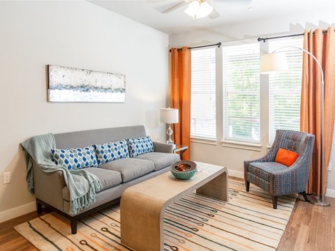 A living room with a grey couch, a blue chair, and a painting on the wall.