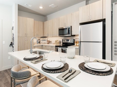 A modern kitchen with a white table set for two.