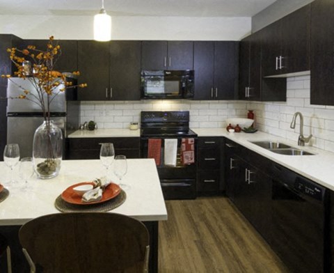 a kitchen with black and white cabinets and a table with wine glasses