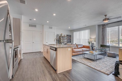 A modern kitchen with a refrigerator on the left and a dining area with a glass table and chairs.