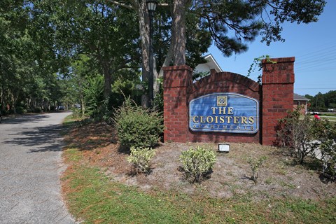 The entrance to The Cloisters with a blue sign on a brick wall. The Cloisters Apartments, 902 67th Avenue North, Myrtle Beach, SC