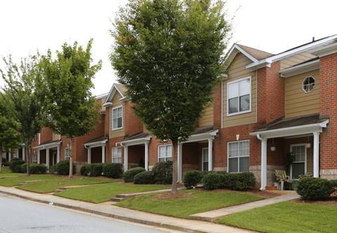 A row of houses with green trees in front.