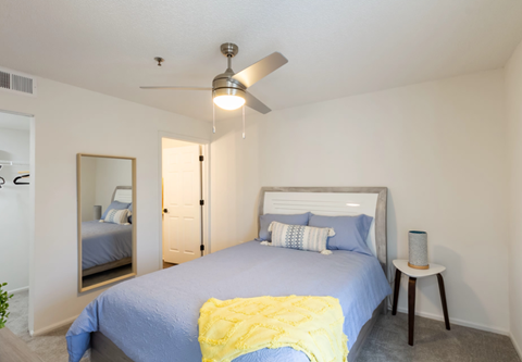 A bedroom with a bed, a ceiling fan, and a nightstand.