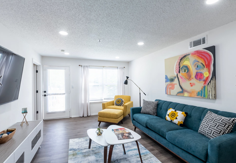 A living room with a blue couch, a yellow chair, and a painting on the wall.
