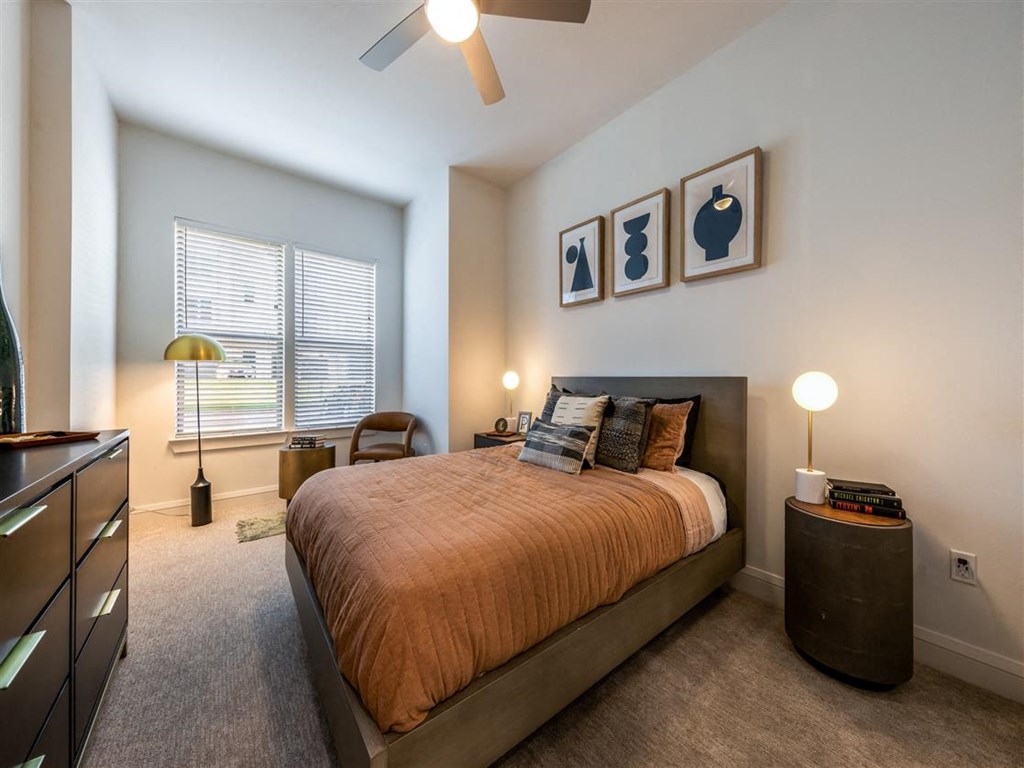 A bedroom with two windows, carpet flooring, and a ceiling fan.