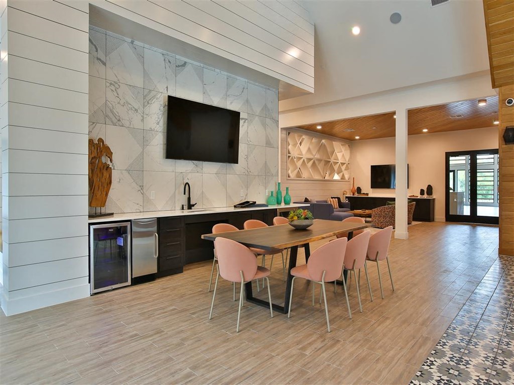 A clubhouse with a community meeting table, charis, a wet bar, and a TV near a lounge area with comfortable seating.