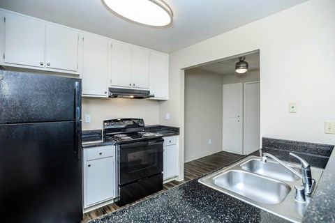 A black fridge sits in a kitchen with white cabinets and a black counter top.