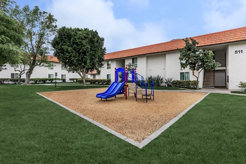 A playground with a blue slide in front of a white building with the number 511 on it.
