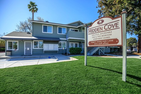 A sign for Hidden Cove Apartments stands in front of a two-story building.