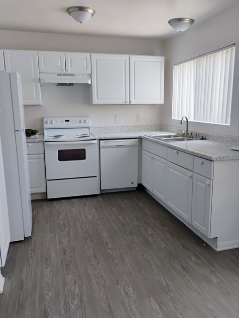 A white kitchen with wood flooring and white appliances.