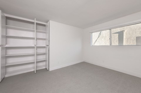 a bedroom with white walls and a window and a closet with shelves