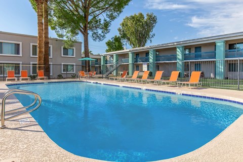 A swimming pool with orange lounge chairs and a building in the background.