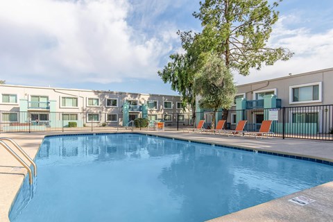 A swimming pool in front of a building with a tree on the side.