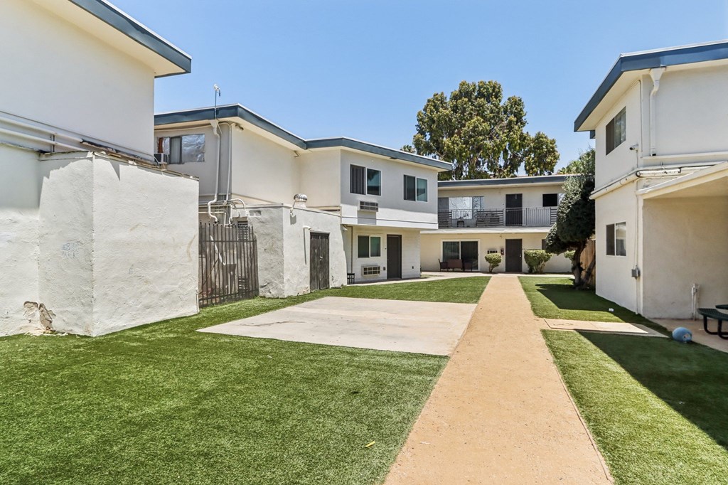 A white building with a long concrete pathway leading to the entrance.