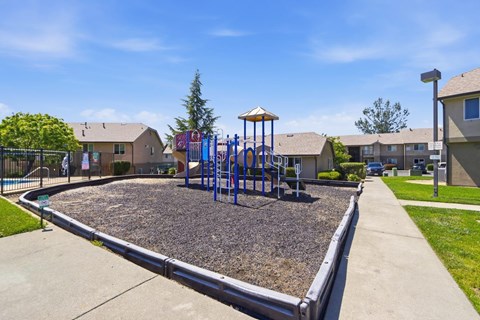 A playground with a swing set and a sandbox in the middle of a grassy area.