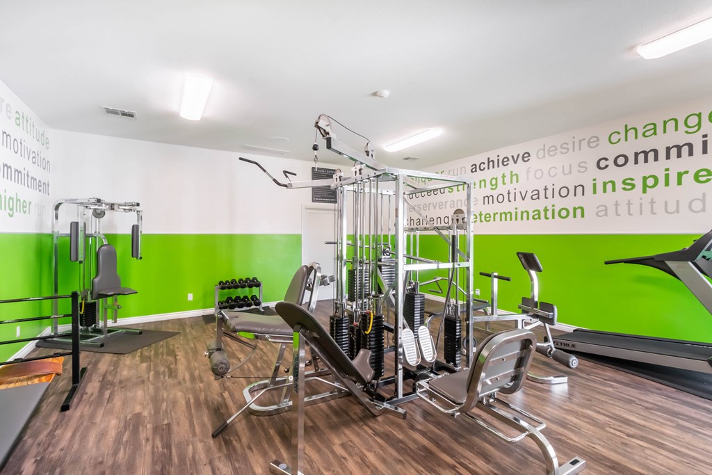 A gym with a green wall and a row of exercise machines at Chaparral Apartments, Palmdale