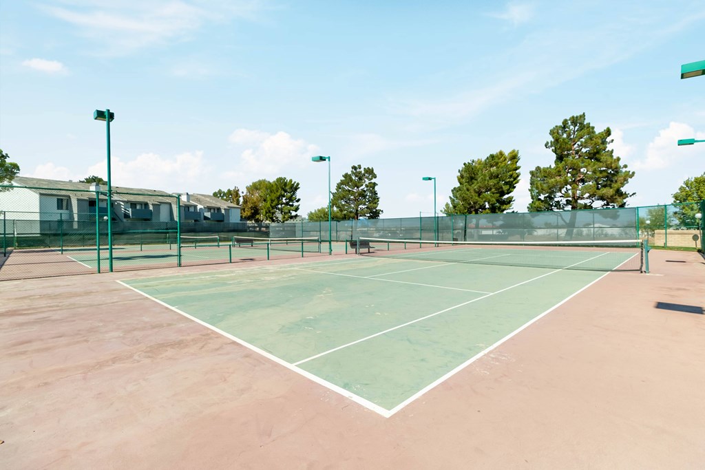 A tennis court with a net and a green fence. at Chaparral Apartments, Palmdale