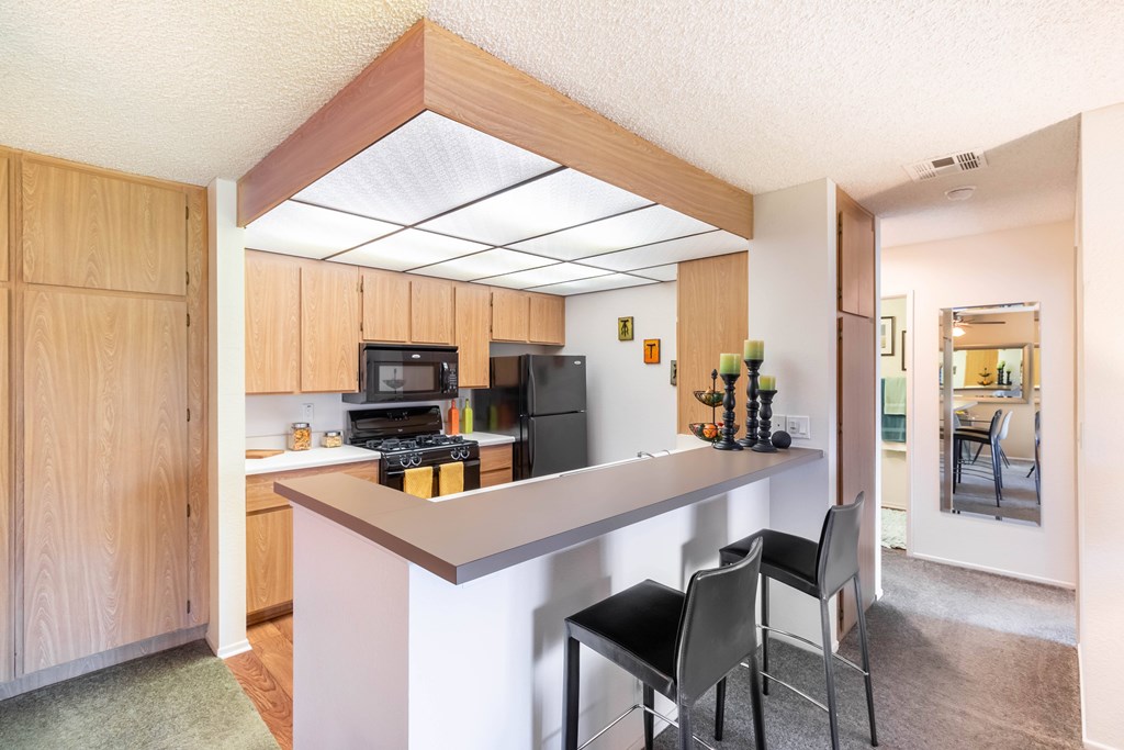 A kitchen with a white counter and black chairs. at Chaparral Apartments, Palmdale, CA, 93551