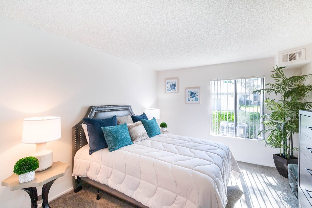 A bedroom with a large bed and a window with blinds at Chaparral Apartments, California, 93551