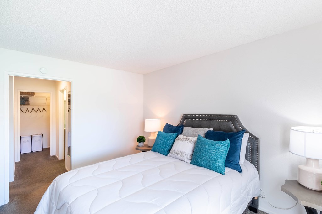 A bedroom with a white bed and blue pillows. at Chaparral Apartments, Palmdale, California