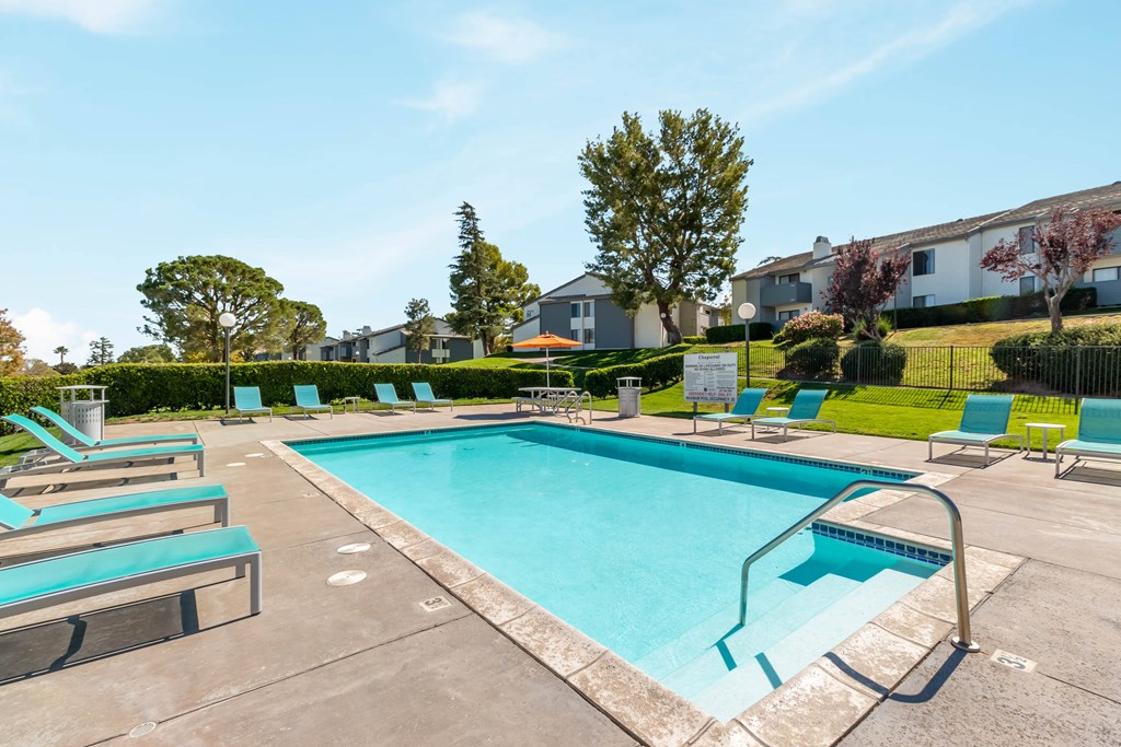 A swimming pool surrounded by lounge chairs and trees. at Chaparral Apartments, Palmdale, California