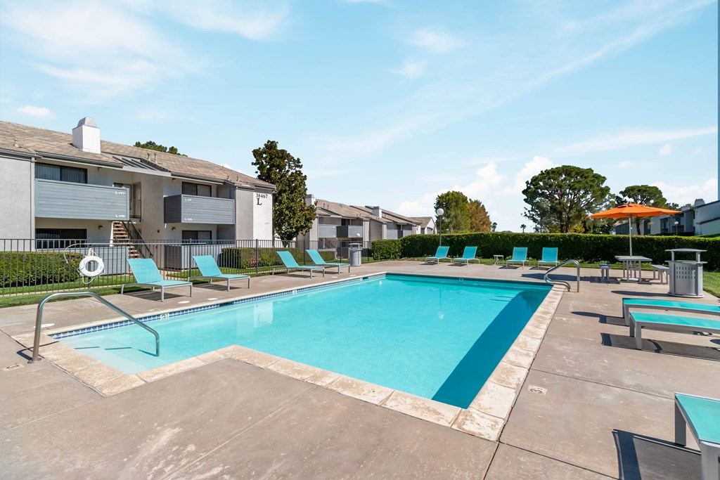 A swimming pool surrounded by lounge chairs and apartment buildings at Chaparral Apartments, Palmdale, CA