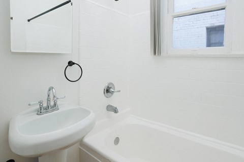 A white sink with a silver faucet is on the left side of a white bathtub.