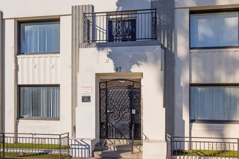 A white building with a black gate and a sign that says 87.