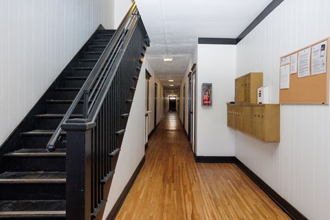 A long hallway with a staircase on the left and a bulletin board on the right.