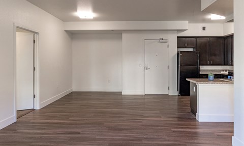 an empty living room with wood flooring and a kitchen