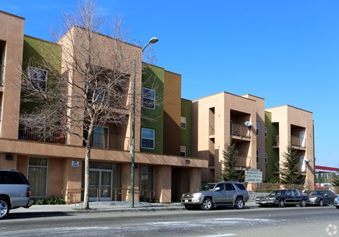 A row of apartment buildings with cars parked in front.