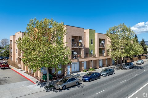 A street view of a multi-story building with cars parked in front.