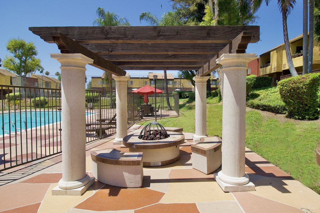 a patio with a fire pit and a pergola overlooking a swimming pool at Brookhollow Apartments, California