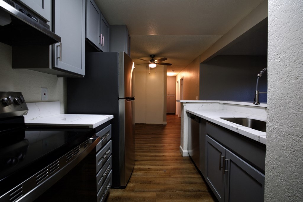a kitchen with black cabinets and a sink and a hallway with a ceiling fan at Brookhollow Apartments, West Covina , California