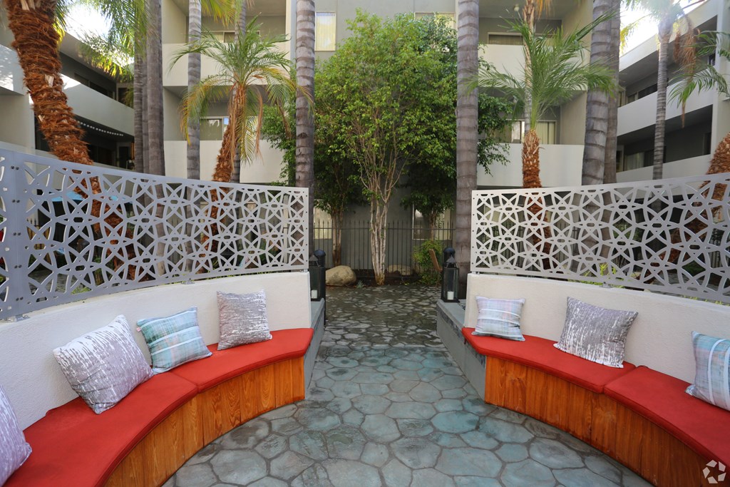 A white bench with red cushions is surrounded by a white lattice fence.