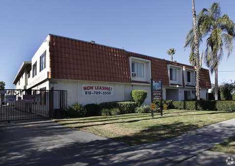 A building with a sign that says "NOW LEASING!" is surrounded by a fence and palm trees.