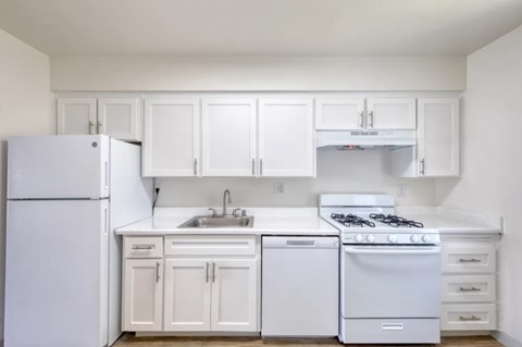 A white kitchen with a refrigerator, sink, and stove.