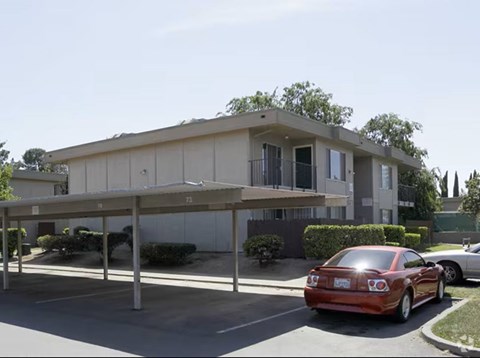 A red car is parked in a parking lot in front of a building.
