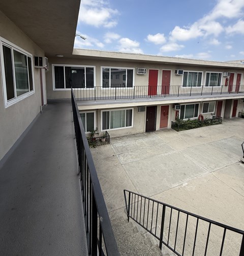 A balcony with a black railing and a view of a building with red and white doors.