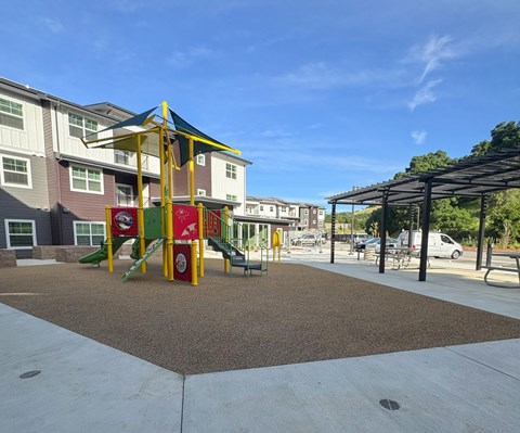 A playground with a yellow and red slide in front of apartment buildings.