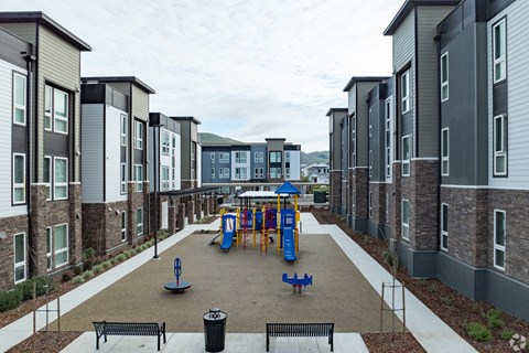 A playground area with a slide and swings is surrounded by apartment buildings.