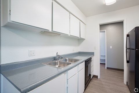 A kitchen with white cabinets and a black fridge.