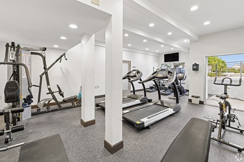 A well-lit gym with a variety of equipment including treadmills, stationary bikes, and weight machines.