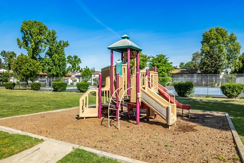 A playground with a red and yellow slide and a green roof.