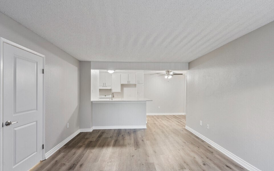 an empty living room and kitchen with white walls and wood flooring at Brookhollow Apartments, West Covina , CA 91792